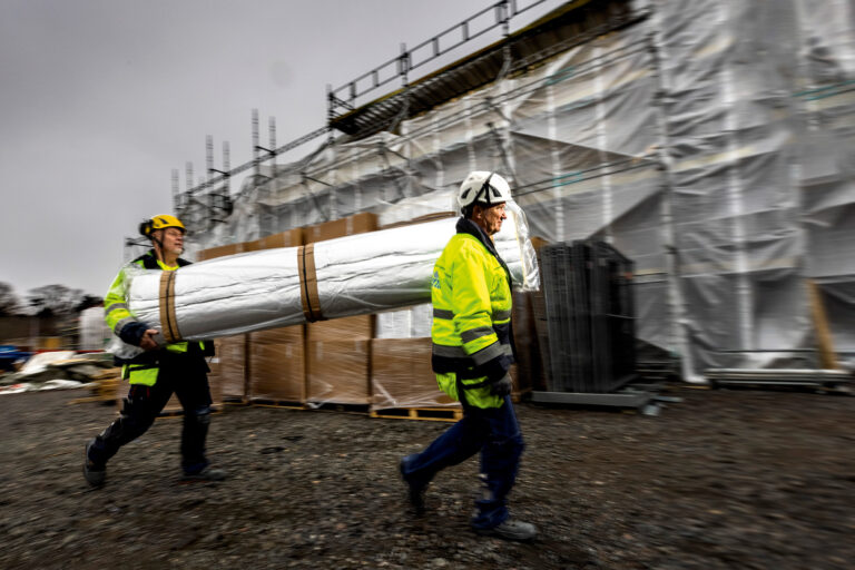 Full fart! Materialet är väldigt lätt. Ventabs Bo Sjöfjord och Bo Malmström har bråttom. I bakgrunden den helt inplastade förskolan Hoppet. Foto: Sören Håkanlind