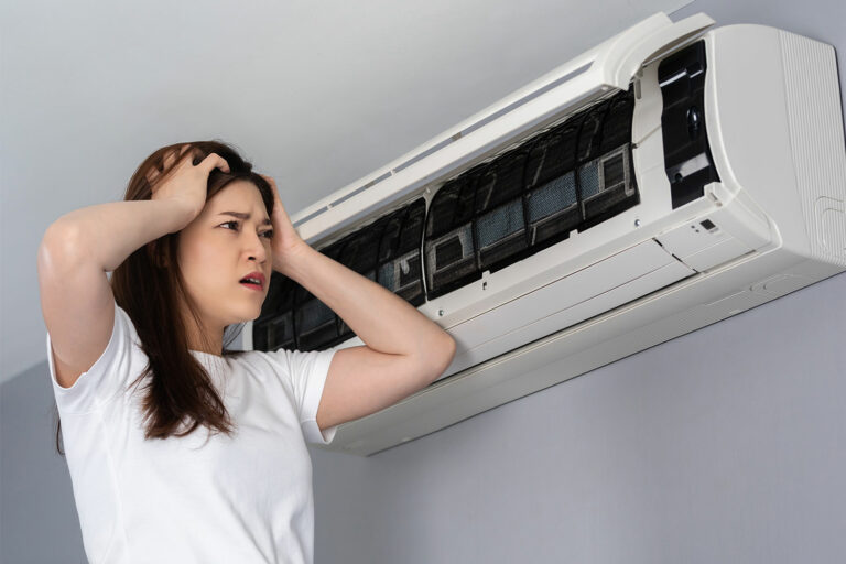 Kvinna bredvid luft/luftvärmepump. Hon är frustrerad över att företaget inte lagar värmepumpen som blåser ut värmen i fel riktning.